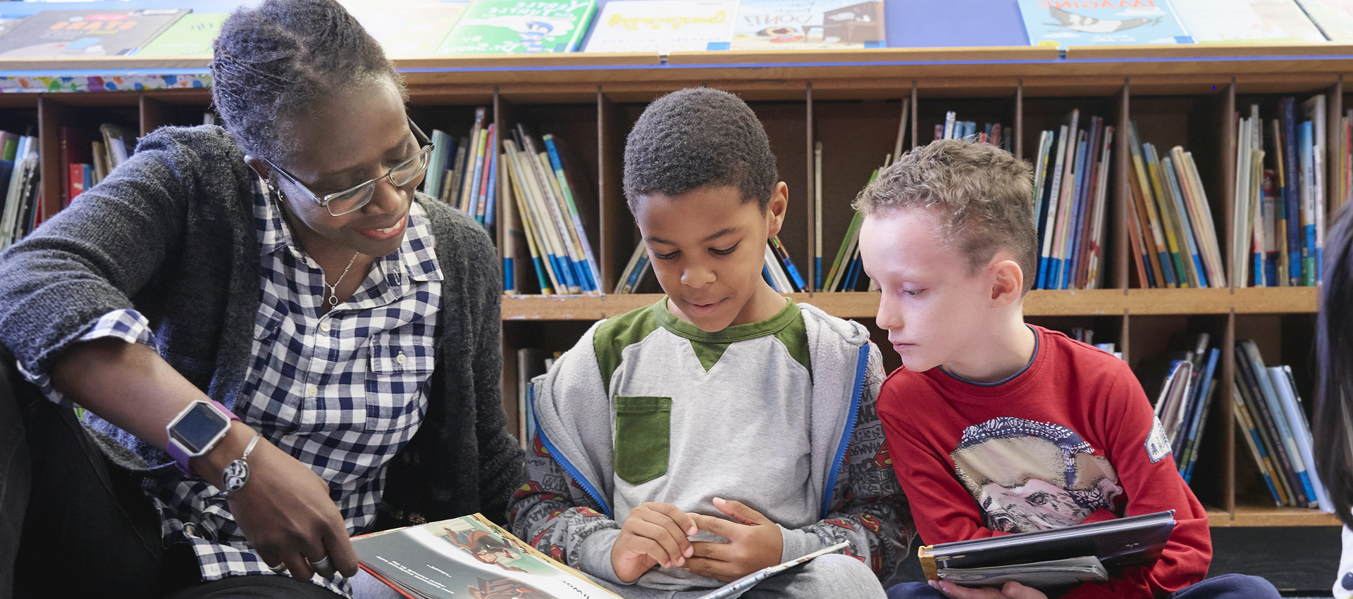 Photo d’une enseignante lisant avec deux jeunes élèves dans une bibliothèque.
